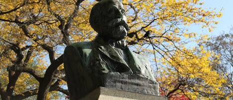 A statue of a man seated at a podium, surrounded by autumn-colored trees.