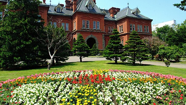 A large red brick building with a green dome and multiple windows. In front, there is a well-maintained garden with various colorful flowers. - Toyoko Inn Hokkaido Sapporo Station Nishi Hokudai Mae (Sapporo)