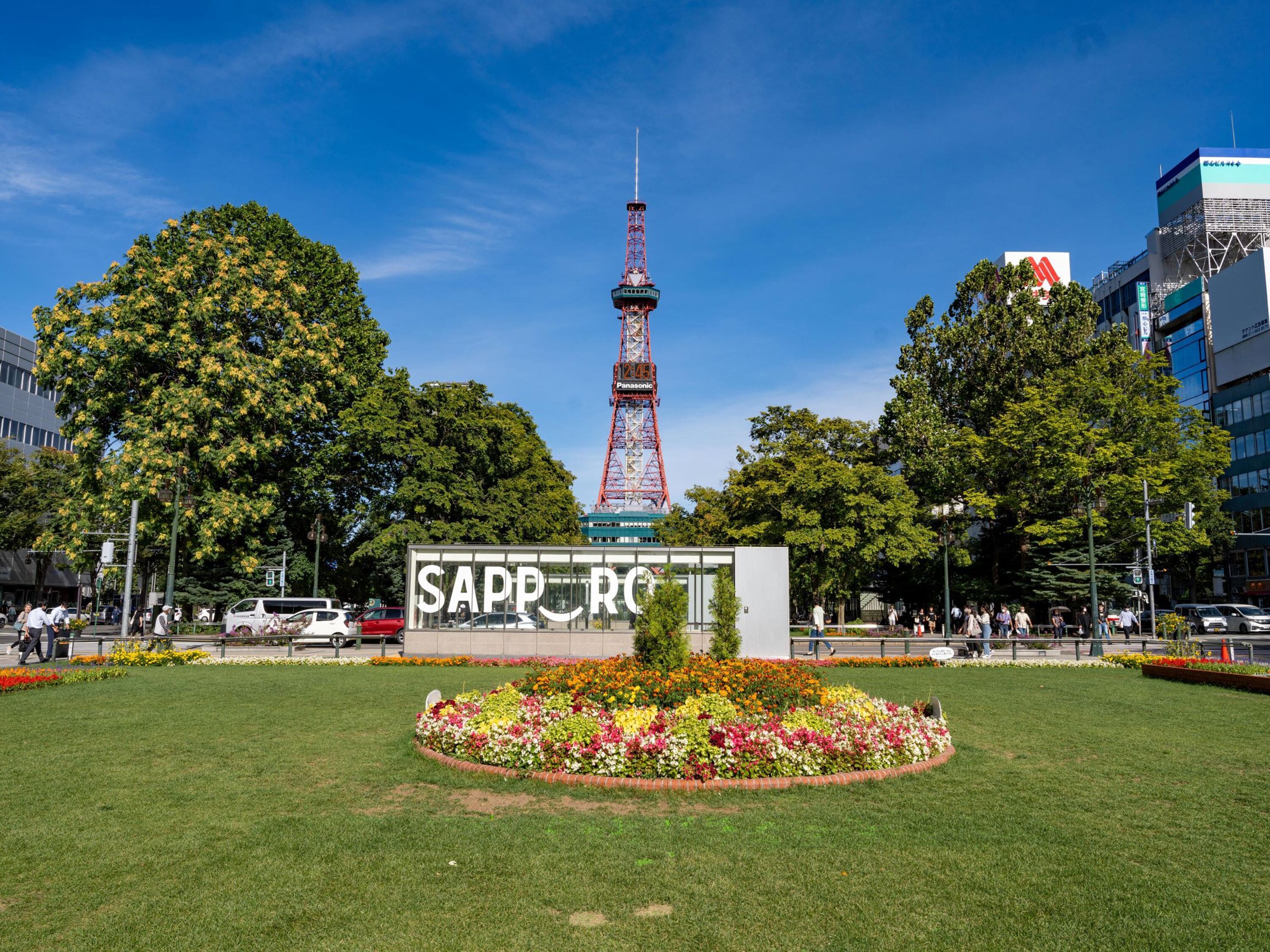 A park with a prominent tower, a sign reading "SAPPORO," and a flower bed.