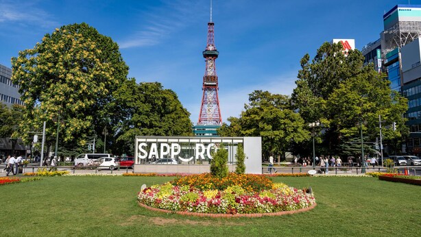 Un parque con una torre destacada, un cartel que dice 'SAPPORO' y una cama de flores.
