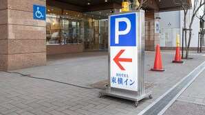 Entrada de un hotel con espacio de estacionamiento para discapacitados, una flecha direccional y un cartel con el nombre del hotel en japonés.
