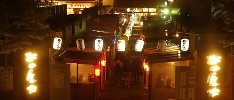 A narrow street with traditional Japanese signage and lanterns, leading to a row of small shops.