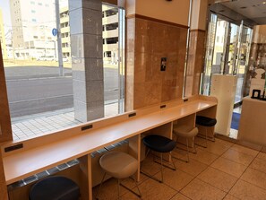 Un hall d’hôtel avec un long comptoir d’accueil, deux chaises, une colonne et une vue sur la rue.