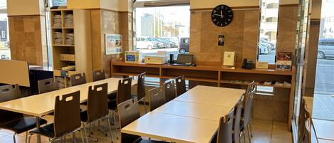 A restaurant with multiple tables and chairs, a clock on the wall, and a window with a view of the street.
