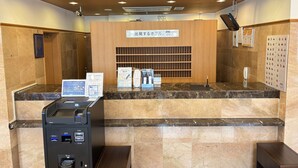 Un área de recepción con mostrador de mármol, un quiosco digital y un letrero que indica un punto de entrega de habitaciones de hotel.