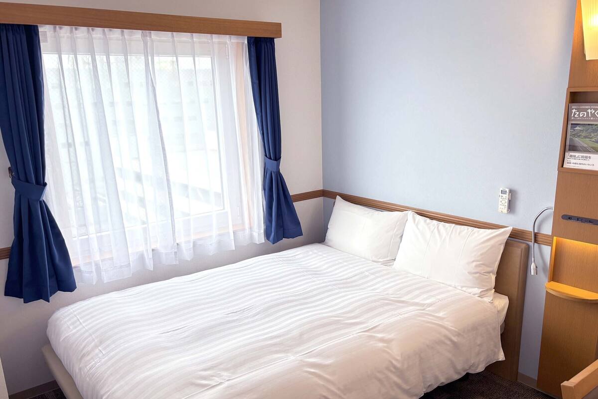 Una habitación de hotel con cama, cortinas, mesita de noche y teléfono instalado en la pared.