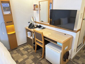 Habitación de hotel con escritorio de madera, un refrigerador pequeño, microondas, teléfono, espejo y televisor.