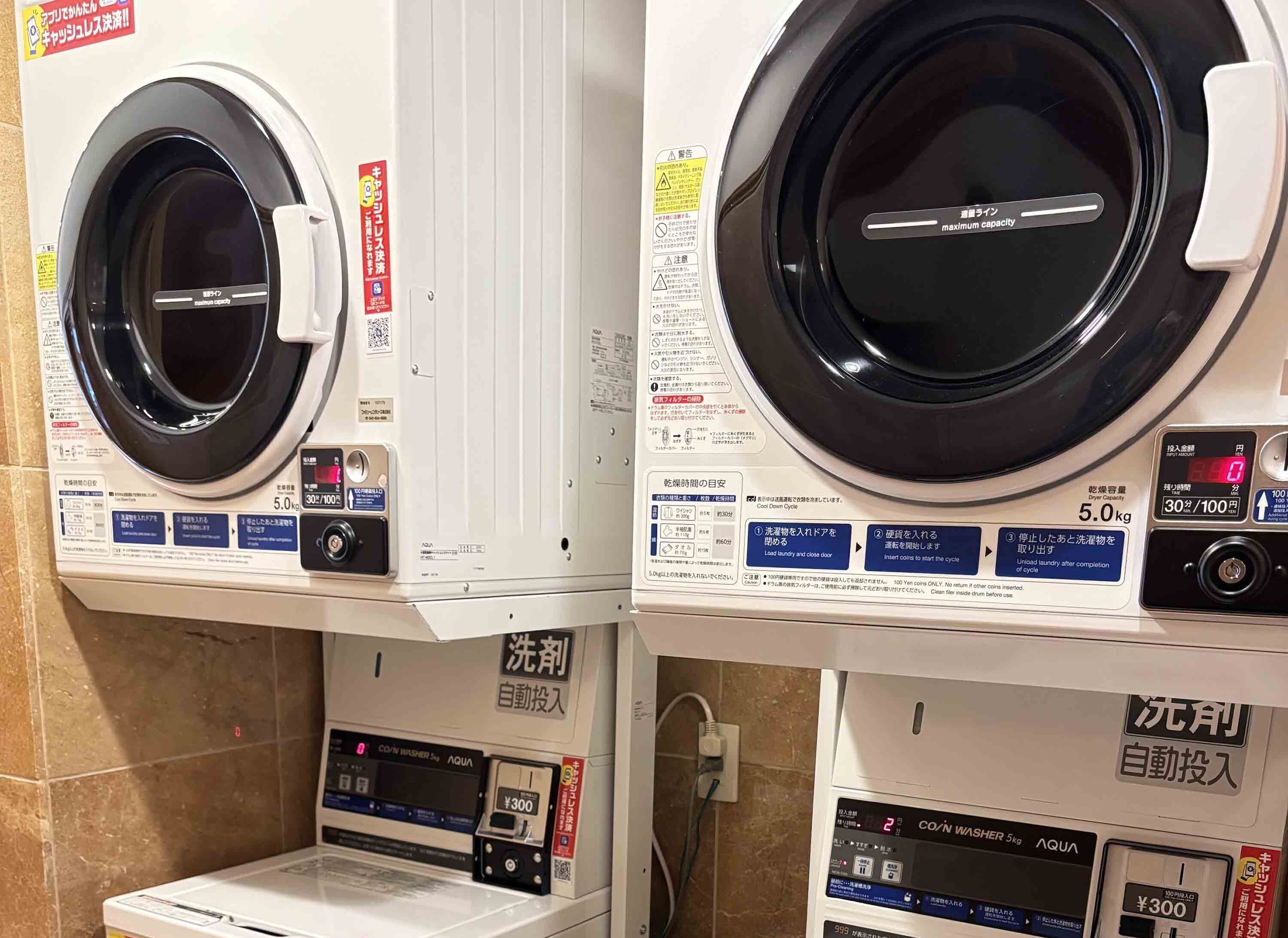 Two front views of a coin-operated laundry machine with a capacity of 5.0 kg, a coin slot, and a control panel with instructions.