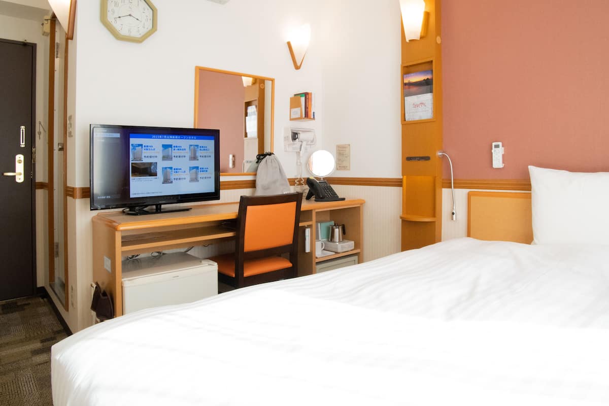 Et hotelværelse med seng, skrivebord, stol, computer og et vægur.