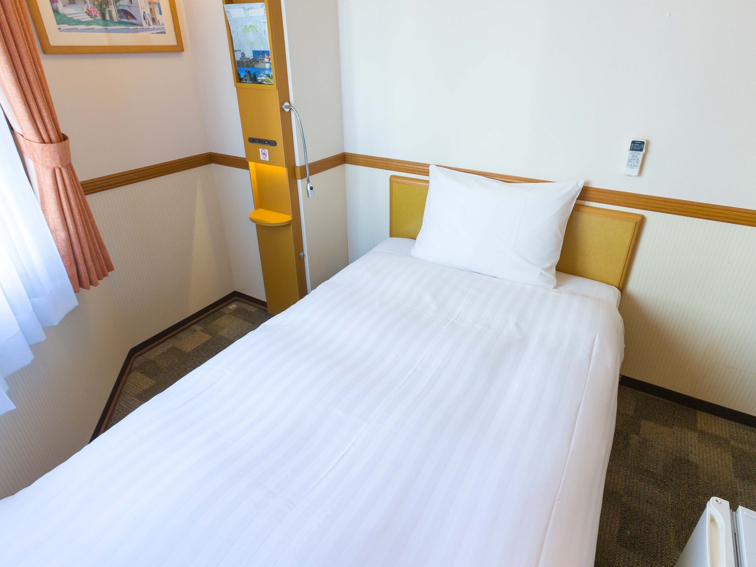 Une chambre d’hôtel avec un lit bien fait, une porte dotée d’un porte-serviettes et un tableau accroché au mur.