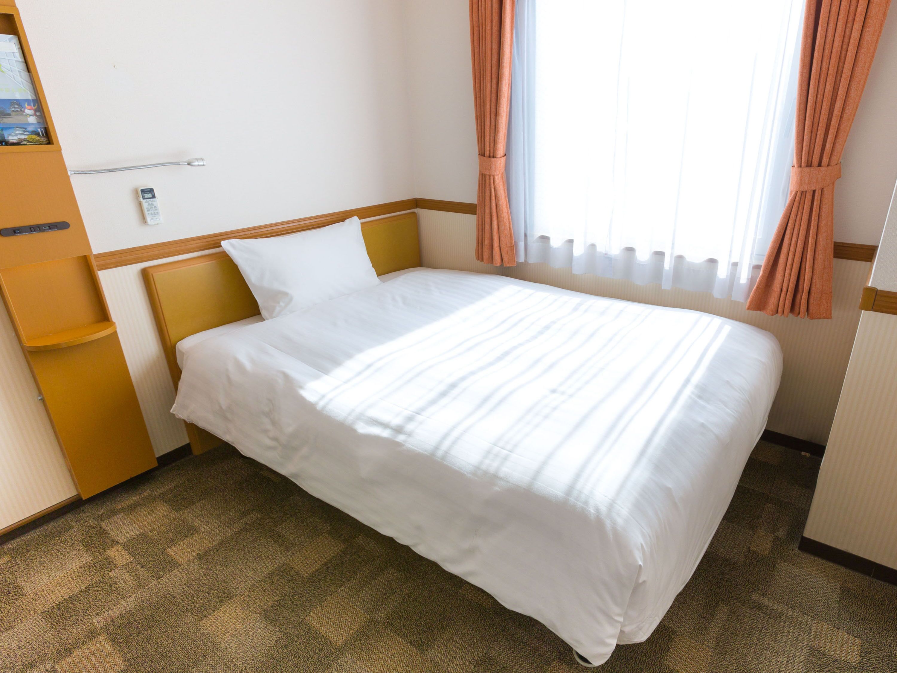A hotel room with a single bed, a wooden headboard, a bedside table, and a window with curtains.