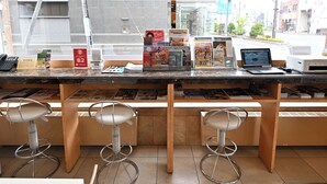 A bar area with a counter displaying various items, a laptop, and a printer. There are three bar stools and a window with a view of the street and buildings. - Toyoko Inn Hokkaido Kushiro Juji Gai (Kushiro)
