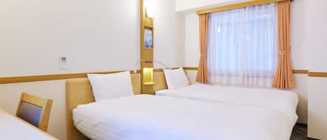 A hotel room with two beds, a desk, a bedside table, a lamp, a window with curtains, and a wall-mounted phone.