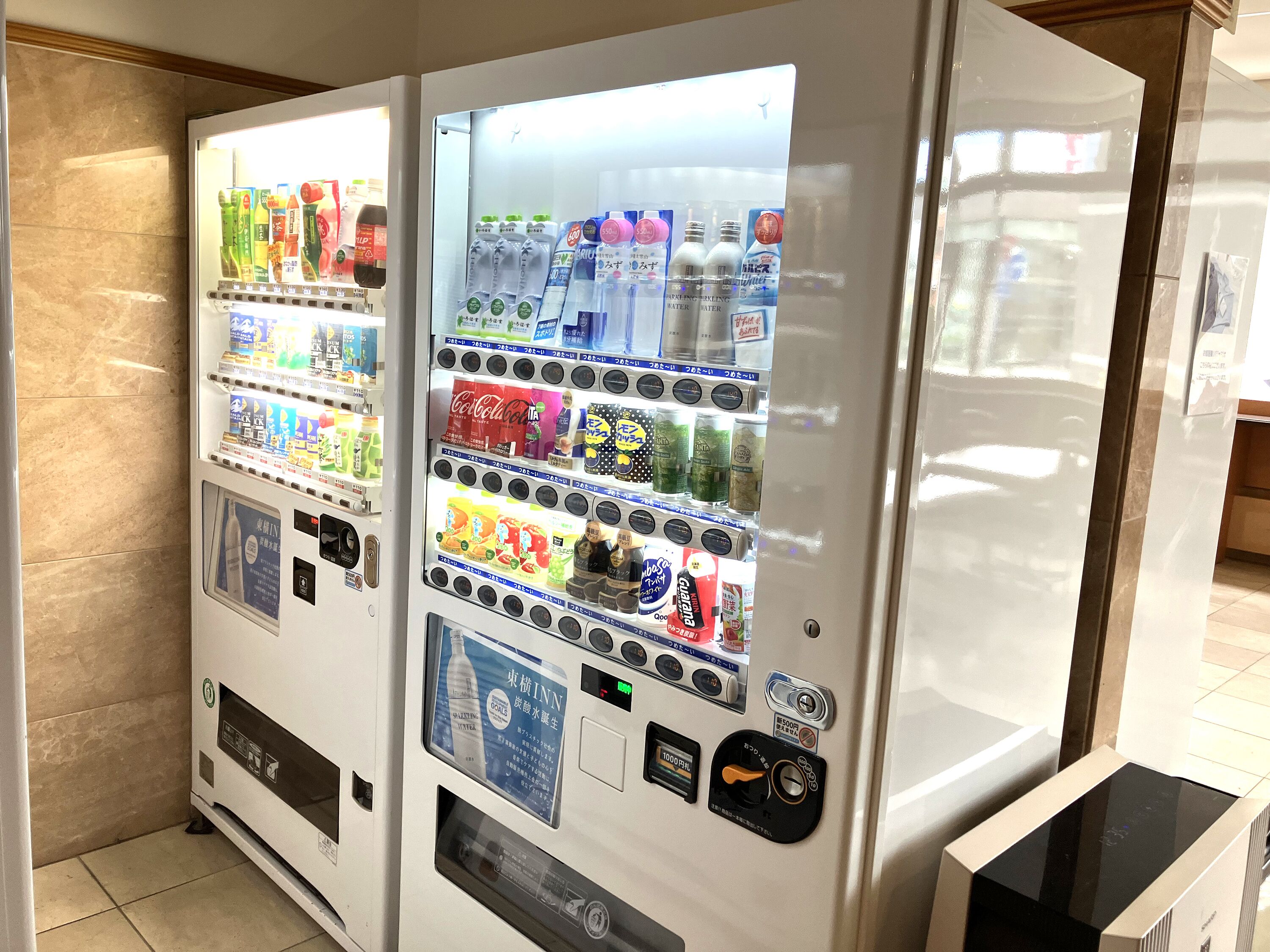 Máquina de vendas com diversas bebidas e lanches, incluindo Coca-Cola e água.