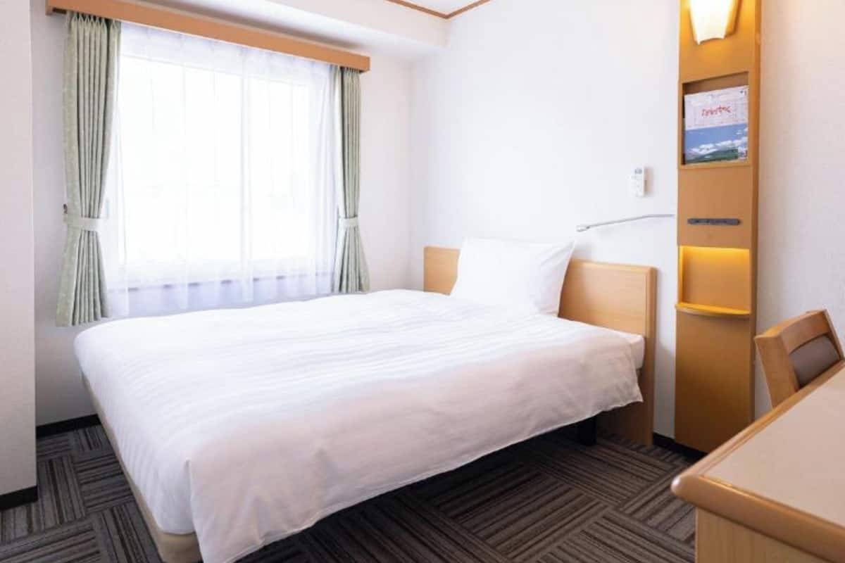 A hotel room with a large bed, a desk, and a window with curtains.