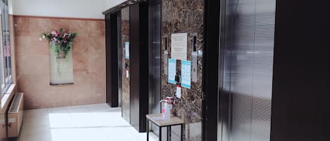 Un pasillo con pared de mármol, un arreglo floral y un ascensor con señalización informativa.