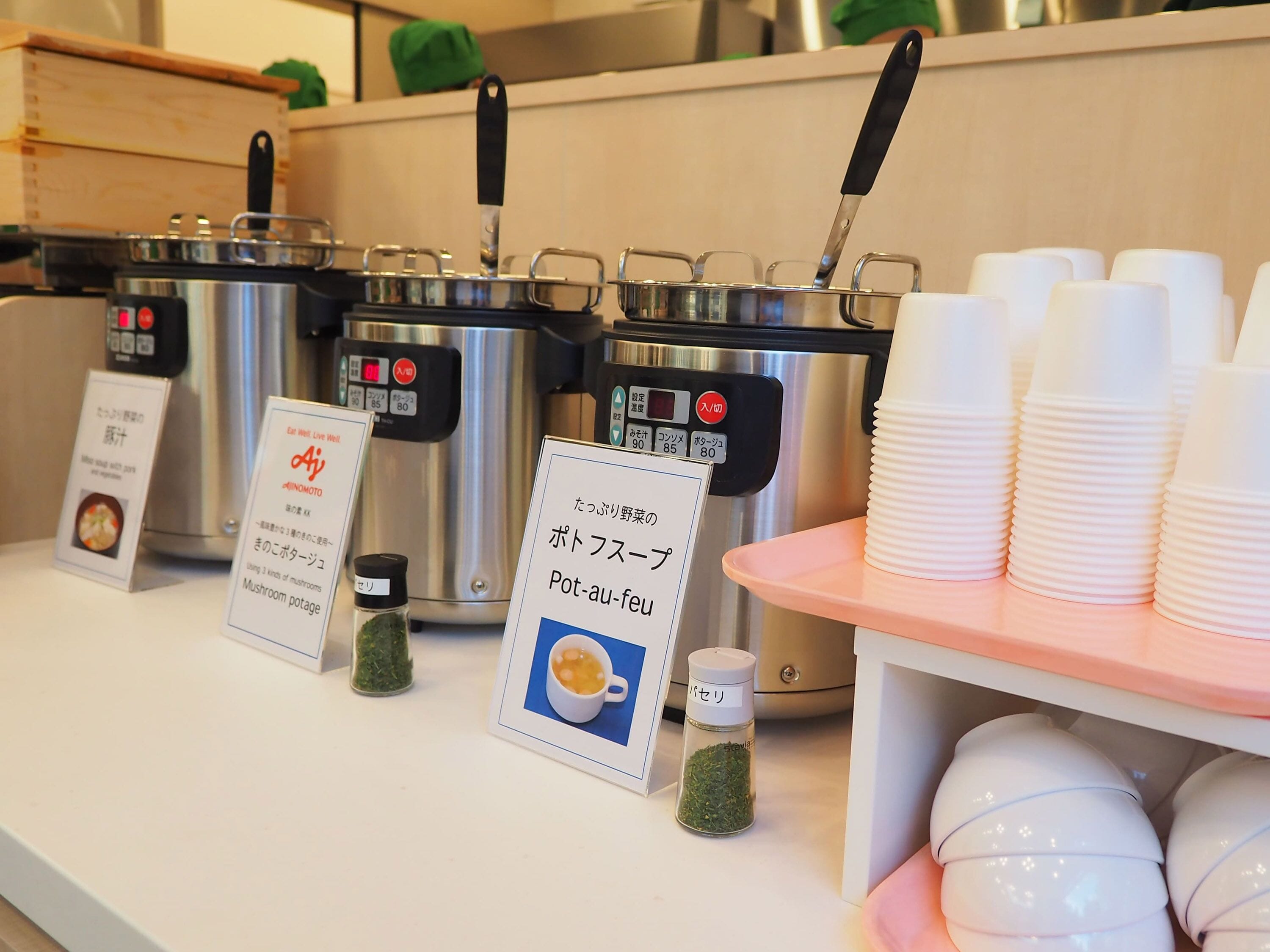 Eine Küchenarbeitsplatte mit mehreren Töpfen, einer Kaffeemaschine und Stapeln Papierbechern.