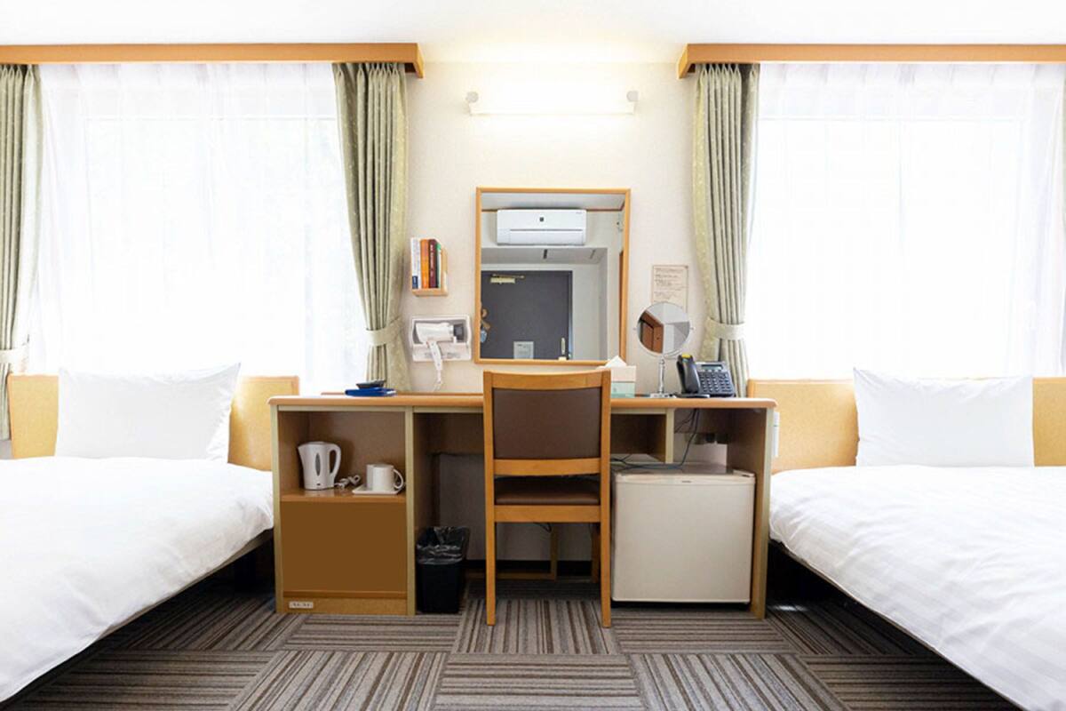 A hotel room with two beds, a desk with a computer, a coffee maker, and a small cabinet.