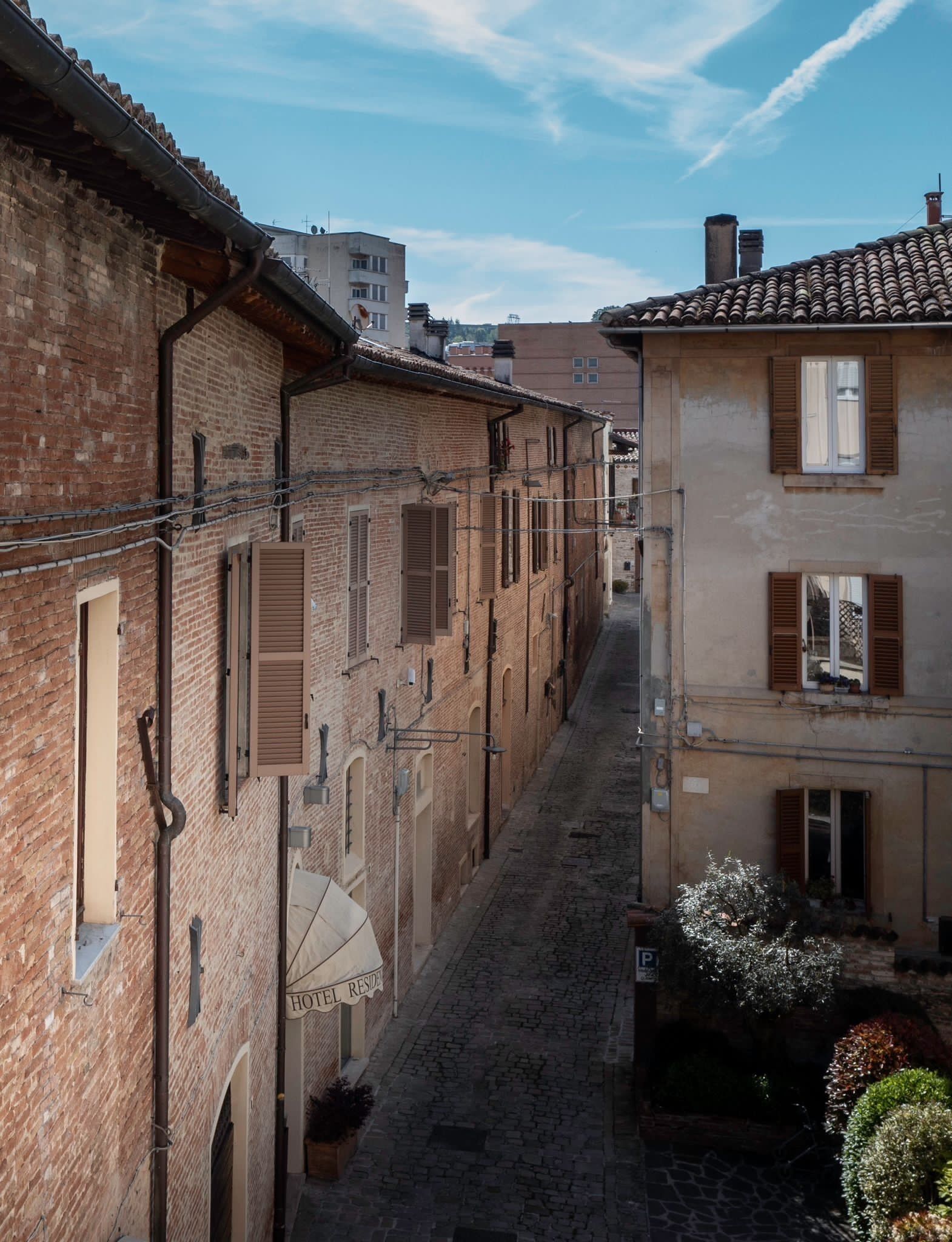 Un estrecho callejón adoquinado flanqueado por edificios de ladrillo tradicionales con ventanas amuralladas y un cartel que indica una residencia hotelera.