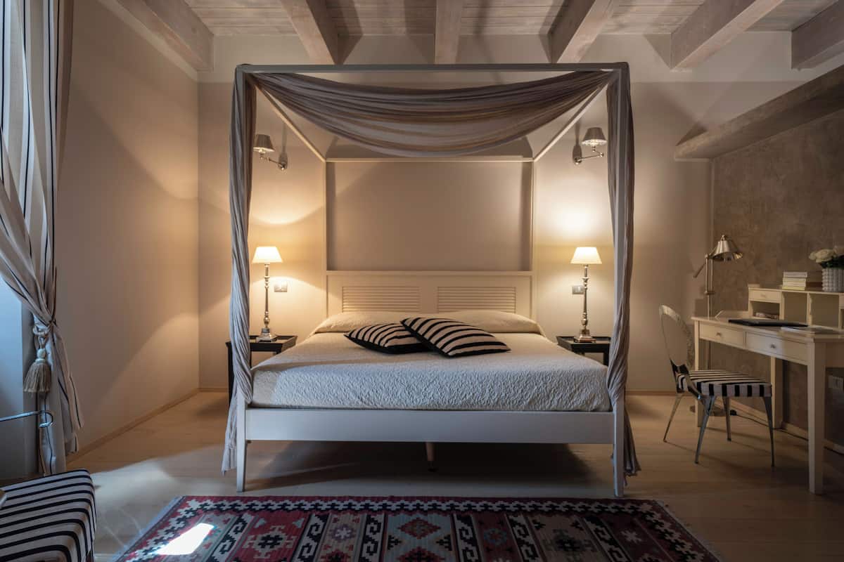 A four-poster canopy bed with two bedside tables, a desk, and a chair in a bedroom.