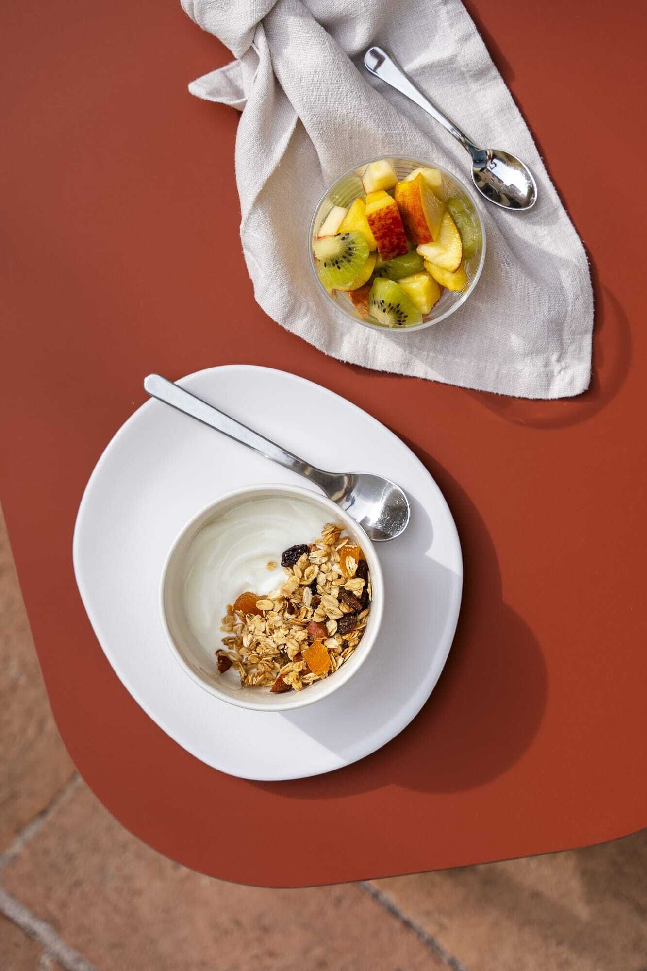A table with a bowl of yogurt and granola, and a bowl of fruit salad on a napkin.