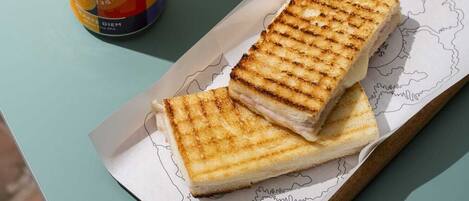 A can of beer, a glass of beer, and a grilled sandwich on a table.