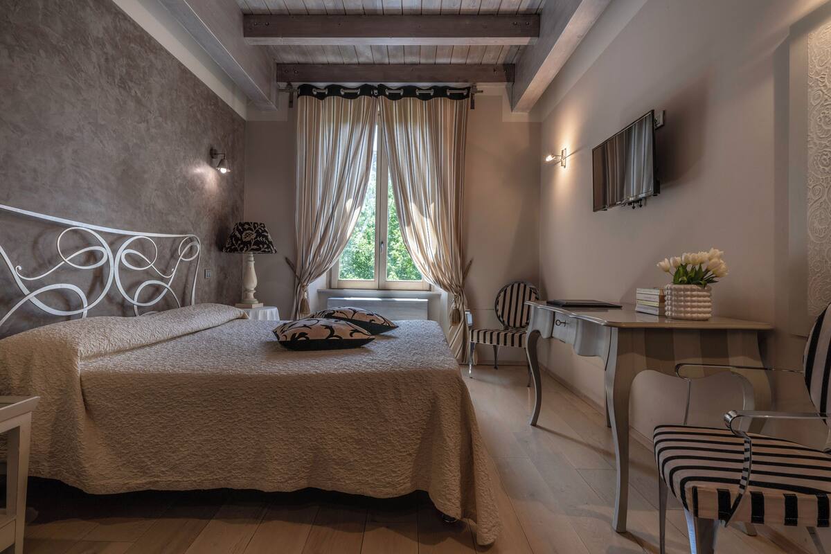 A bedroom with a bed, a desk, a chair, and a window with curtains.