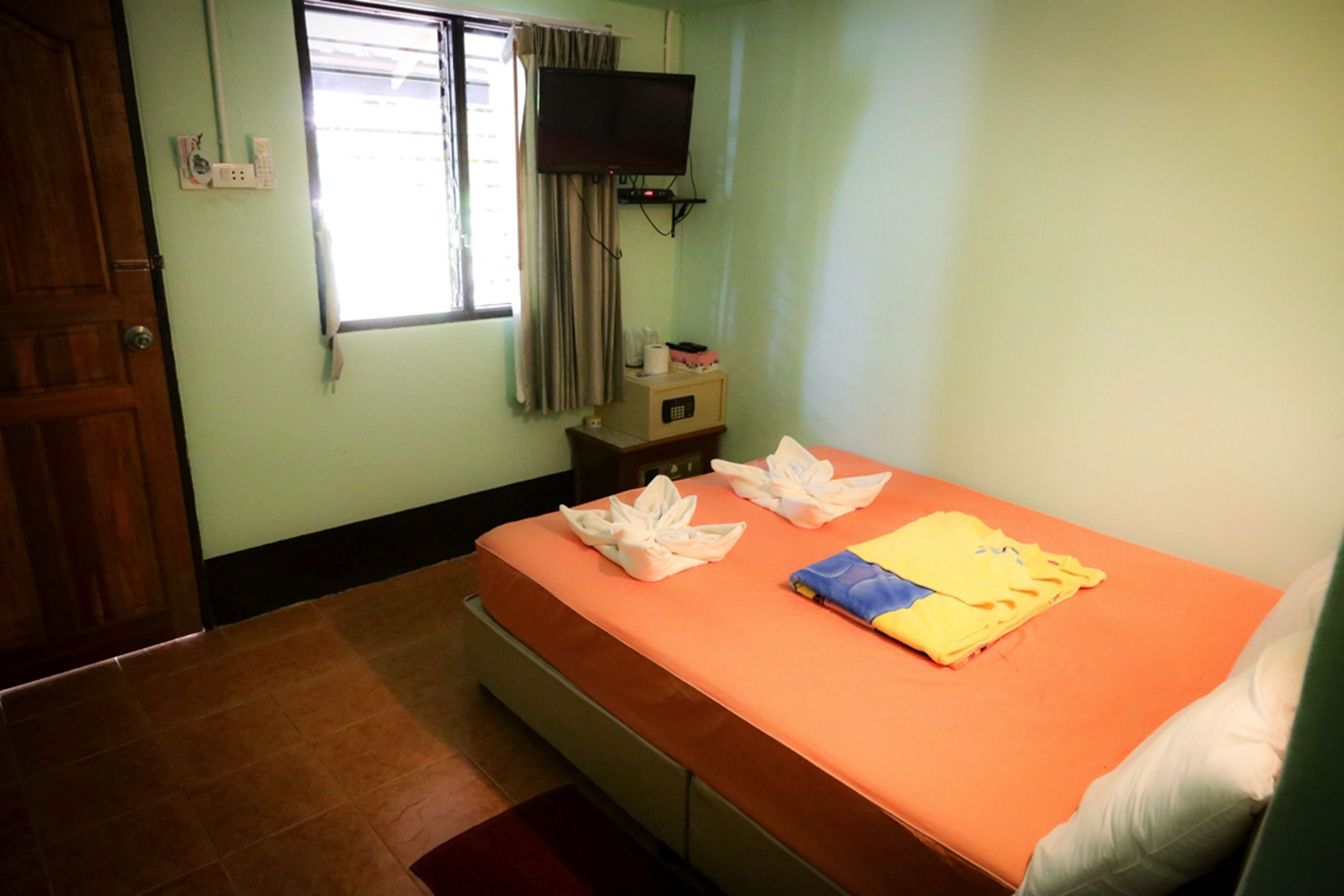A room with a bed, a television mounted on the wall, and a window with curtains.