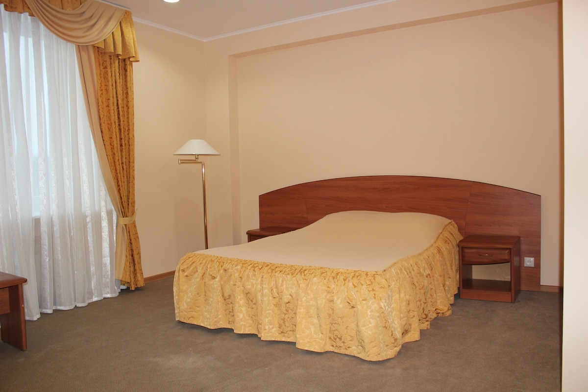 A hotel room with a wooden bed, a nightstand, a lamp, and a window with curtains.