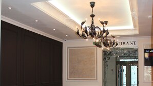 A lobby with a brown leather sofa, a patterned rug, a chandelier, and a sign reading "RESTAURANT".