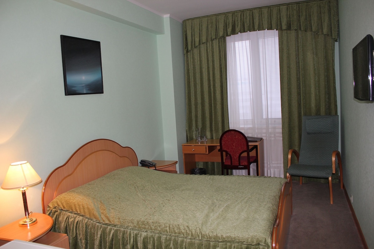 A hotel room with a bed, a desk, a chair, and a television on the wall.
