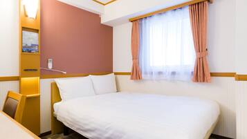 Habitación de hotel con una cama grande, un escritorio, una silla, una mesita de noche, un teléfono en la pared y una ventana con cortinas.