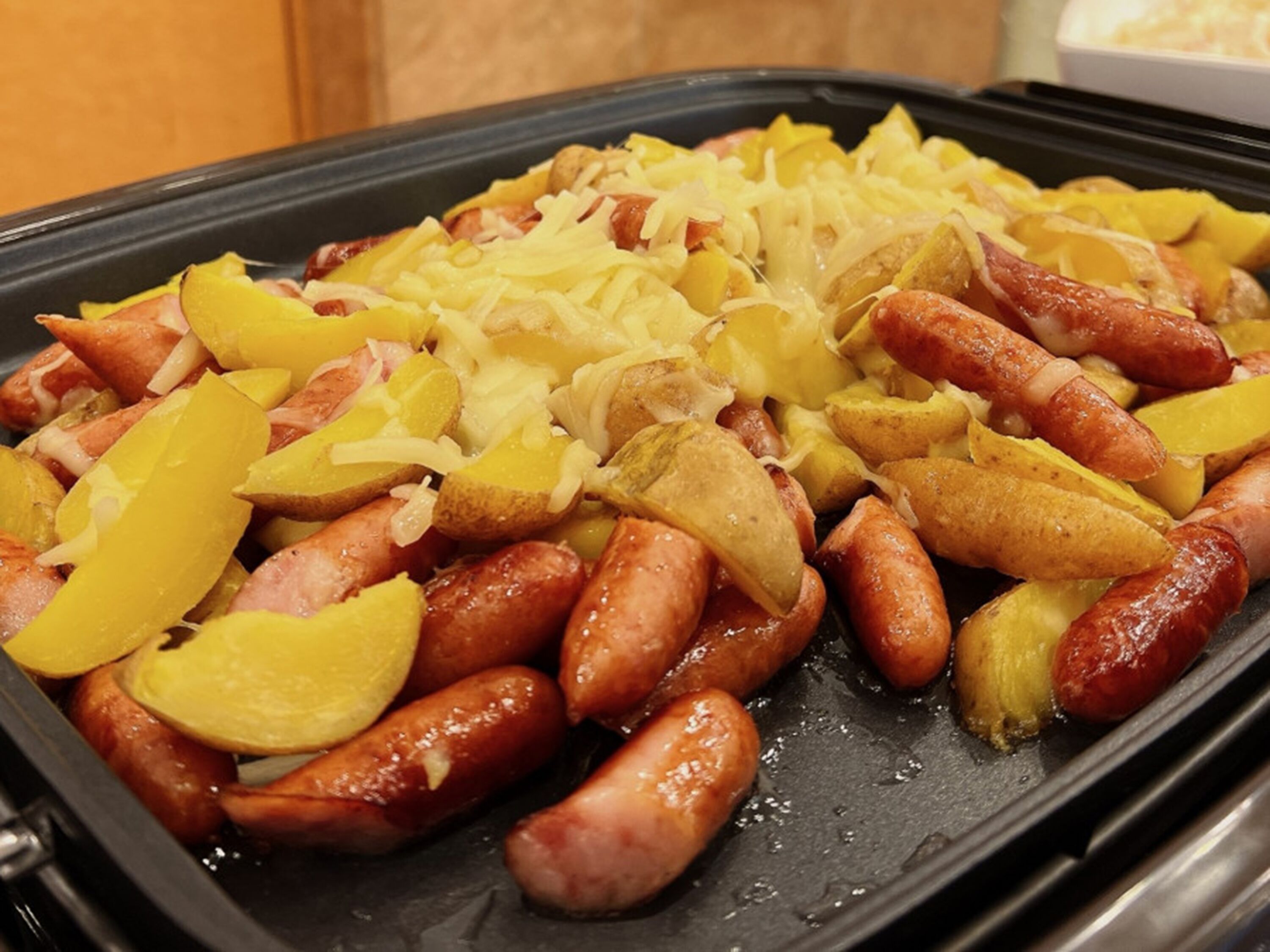 A tray of food with sausages, potatoes, and cheese.