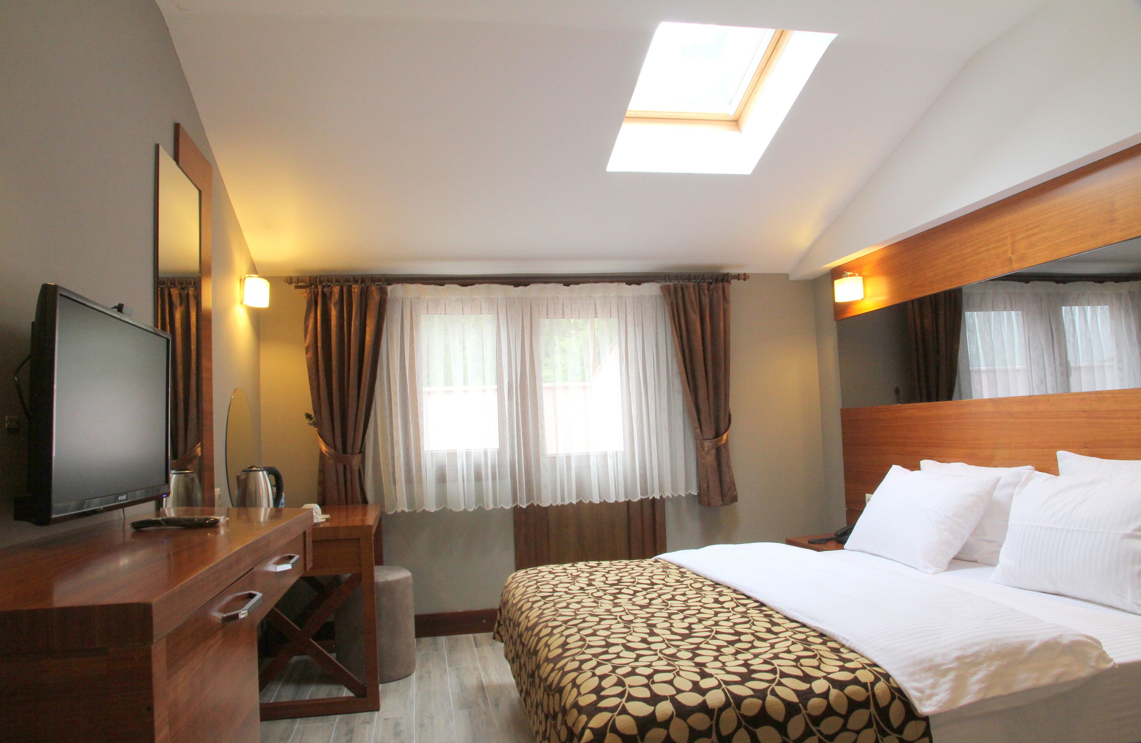 A hotel room with a bed, a desk with a television, a mirror, and a window with curtains.