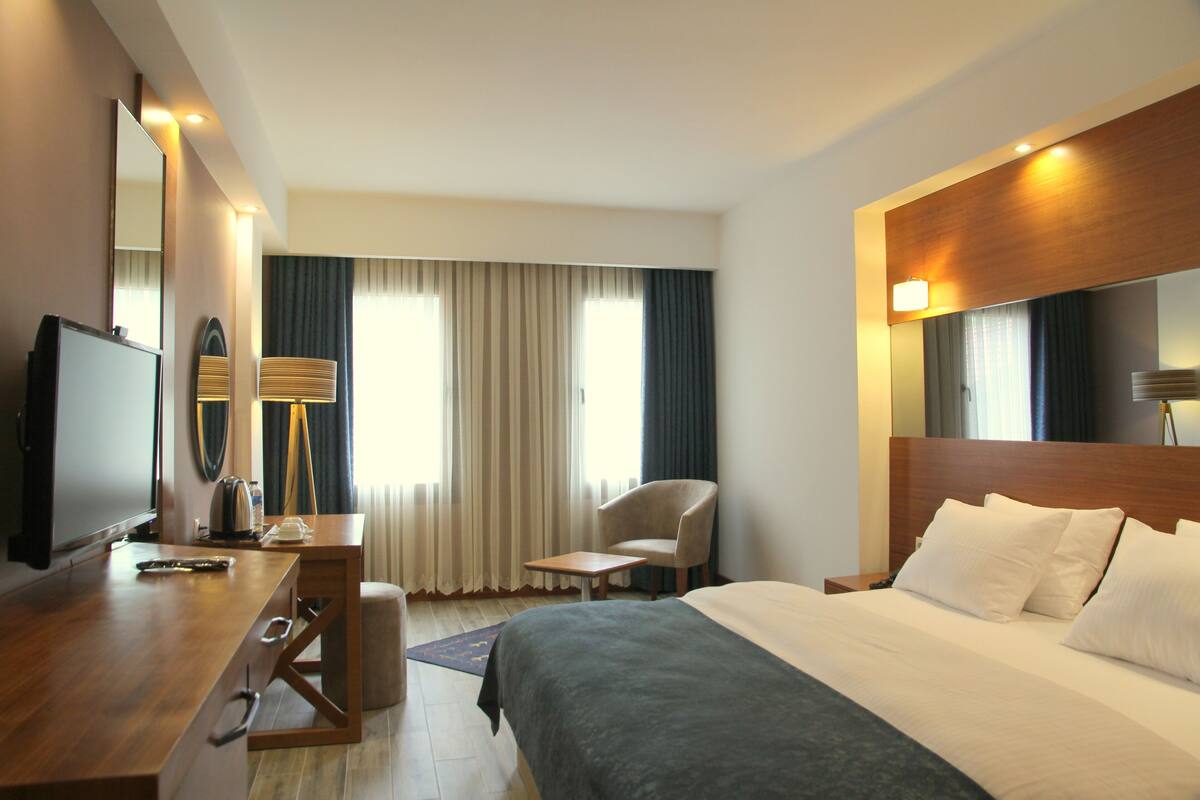 A hotel room with a bed, a desk with a television, a chair, and a large mirror.