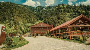 A hotel with a red facade, a large entrance, and a mountainous backdrop. - Kilpa Hotel (Çaykara)