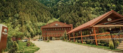 A hotel with a red facade, a large entrance, and a mountainous backdrop.