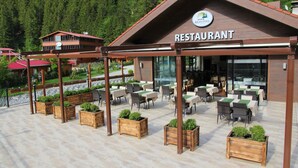 A restaurant with outdoor seating, wooden planters, and a view of a forested area. - Kilpa Hotel (Çaykara)