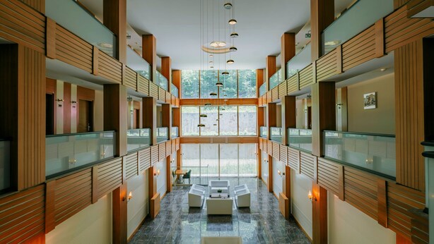 A modern hotel lobby with a central seating area, glass railings, and wooden paneling. - Kilpa Hotel (Çaykara)
