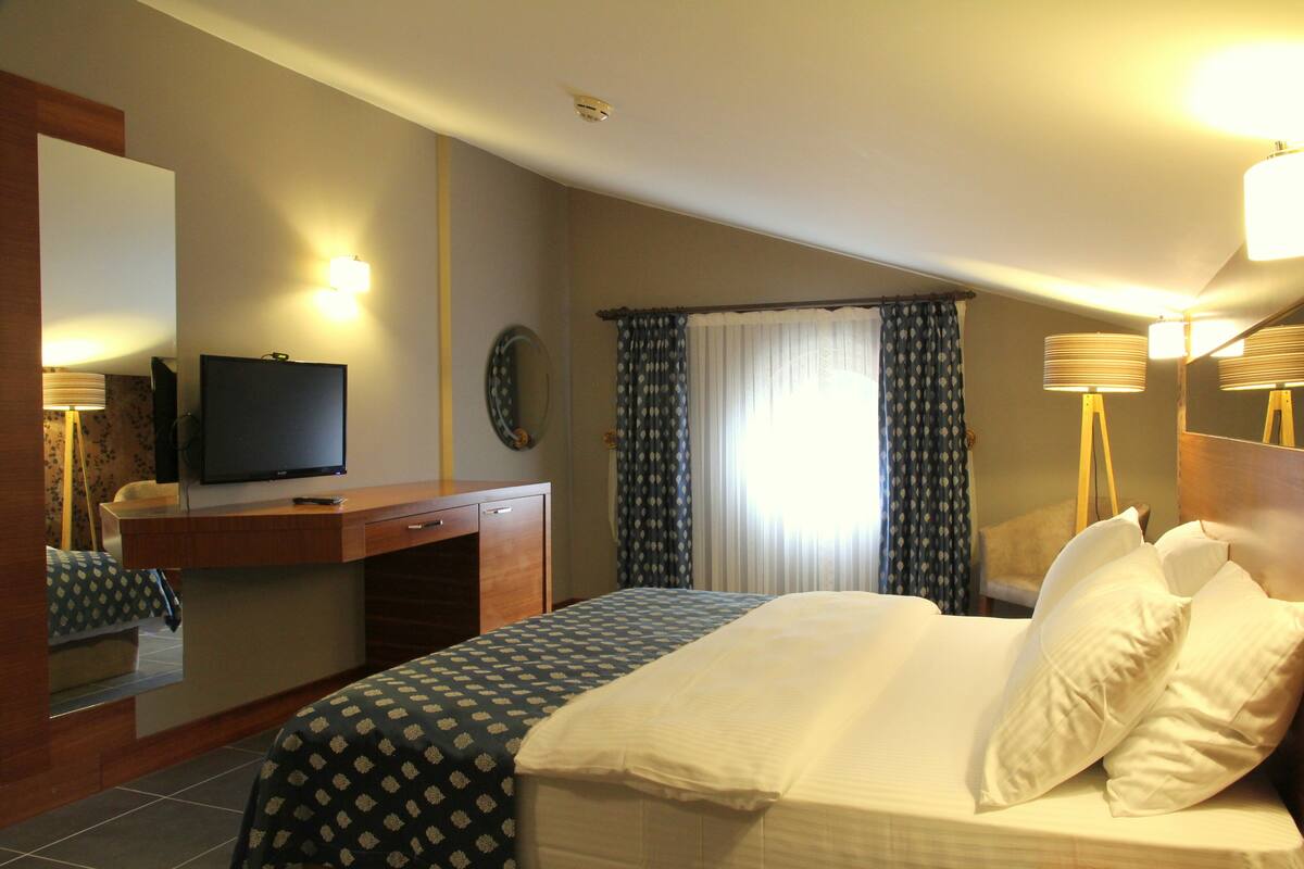 A hotel room with a bed, a desk with a television, a mirror, and two bedside lamps.