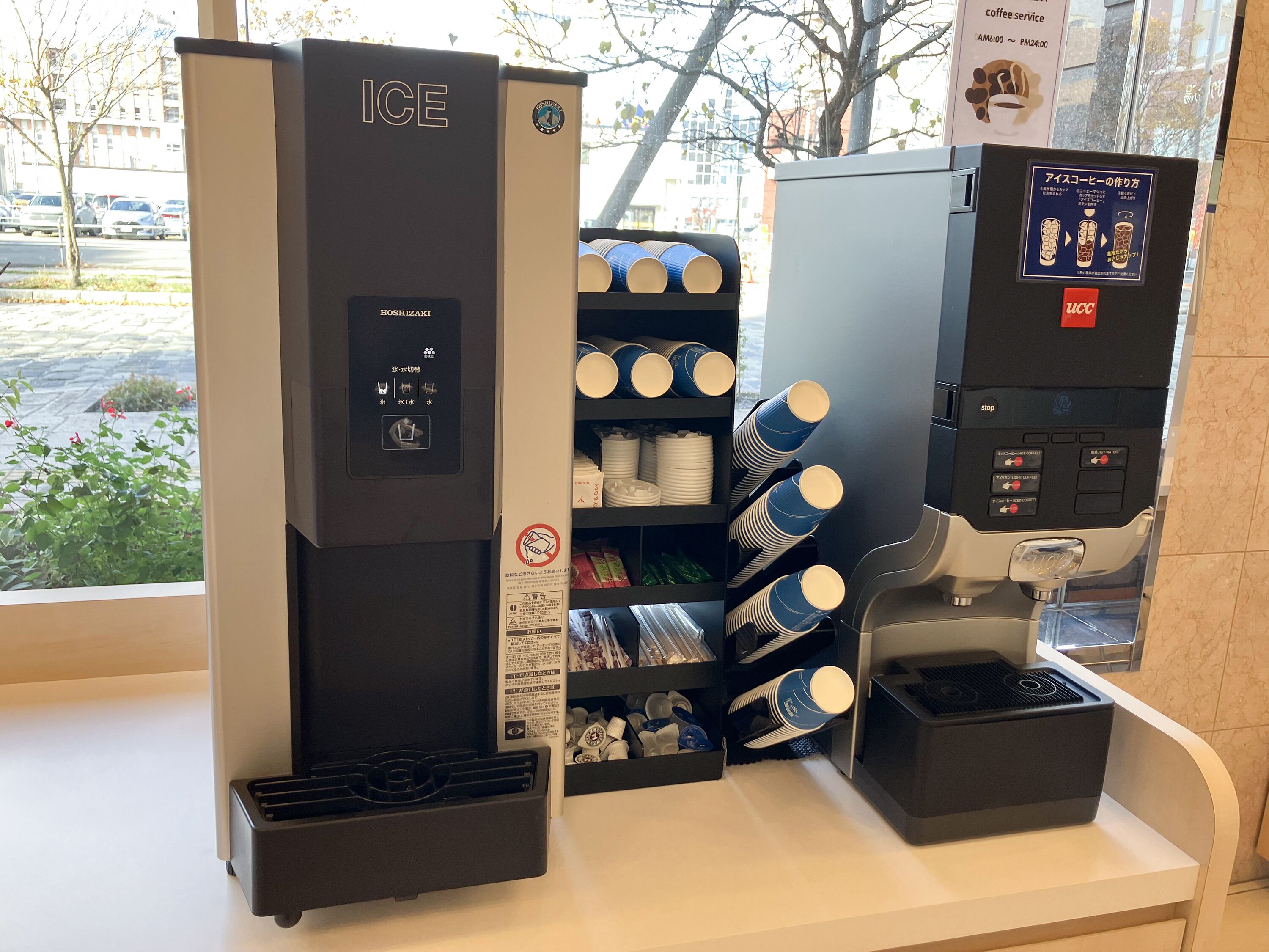 Une machine à café avec un panneau indiquant le service de café, un distributeur automatique et un présentoir de gobelets jetables.