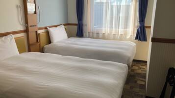 A hotel room with two beds, a wooden headboard, a window with blue curtains, and a wall-mounted phone.