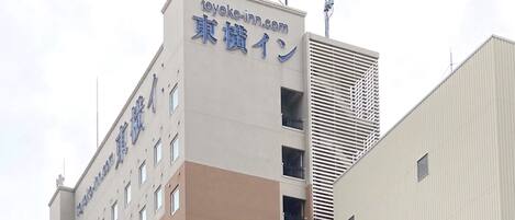 Un edificio con un cartel que indica que es un hotel Toyoko Inn y muestra las direcciones toyokoinn.com y 東横イン.