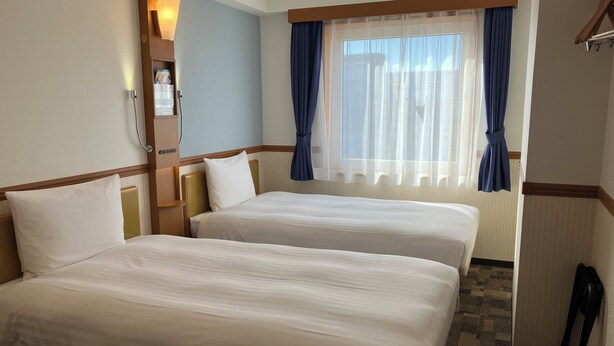 A hotel room with two beds, a bedside table, a lamp, a window with curtains, and a coat rack. - Toyoko Inn Hokkaido Asahikawa Station Higashi (Asahikawa)