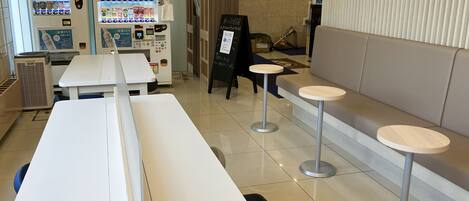 Interior de una cafetería moderna y limpia, con máquinas expendedoras, zonas de estar y una barra.