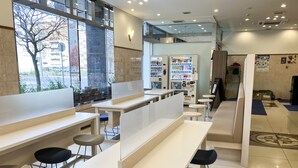 A modern cafe with white tables and chairs, vending machines, and a view of the street outside. - Toyoko Inn Hokkaido Asahikawa Station Higashi (Asahikawa)