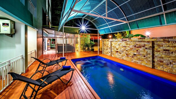 Une piscine intérieure dotée d’une terrasse en bois et de chaises longues, entourée d’un mur de briques et protégée par une paroi en verre.
