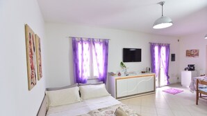 A hotel room with a bed, a desk, a TV, and purple curtains. - IzzHome Regina Margherita (Pula)