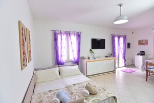 Habitación de hotel con cama, escritorio, televisor y cortinas moradas.