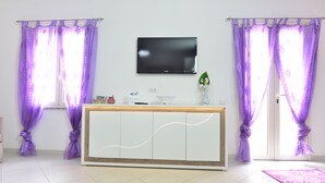A modern living room with a white entertainment unit, a flat-screen TV mounted above it, and purple curtains. - IzzHome Regina Margherita (Pula)
